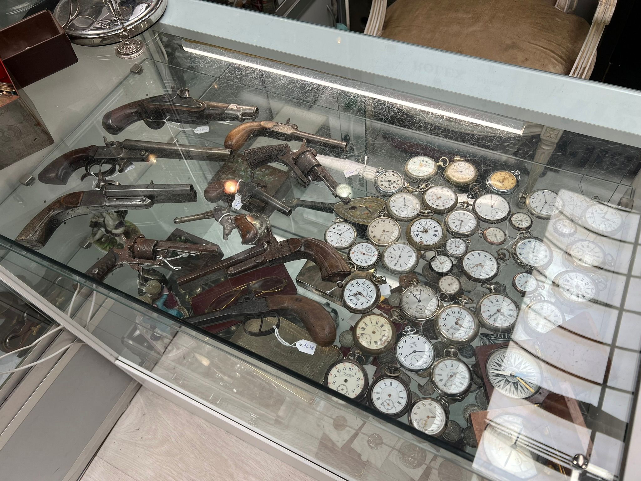 Vitrine de stand avec pistolets anciens à poudre noire et montres à gousset en argent